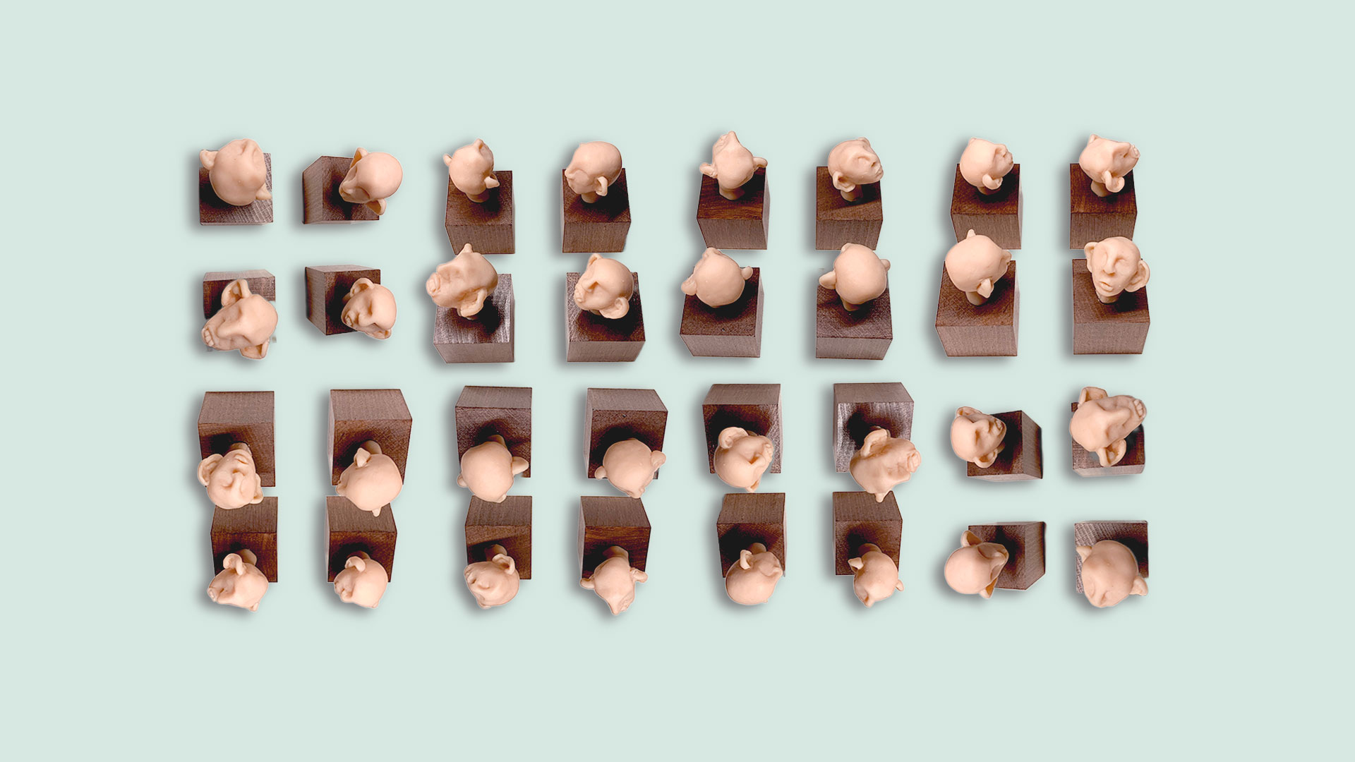 Mehrere Lauscher-Figuren mit grossen Ohren stehen in Reihen auf kleinen Holzsockeln vor hellgrünem Hintergrund, von oben betrachtet.