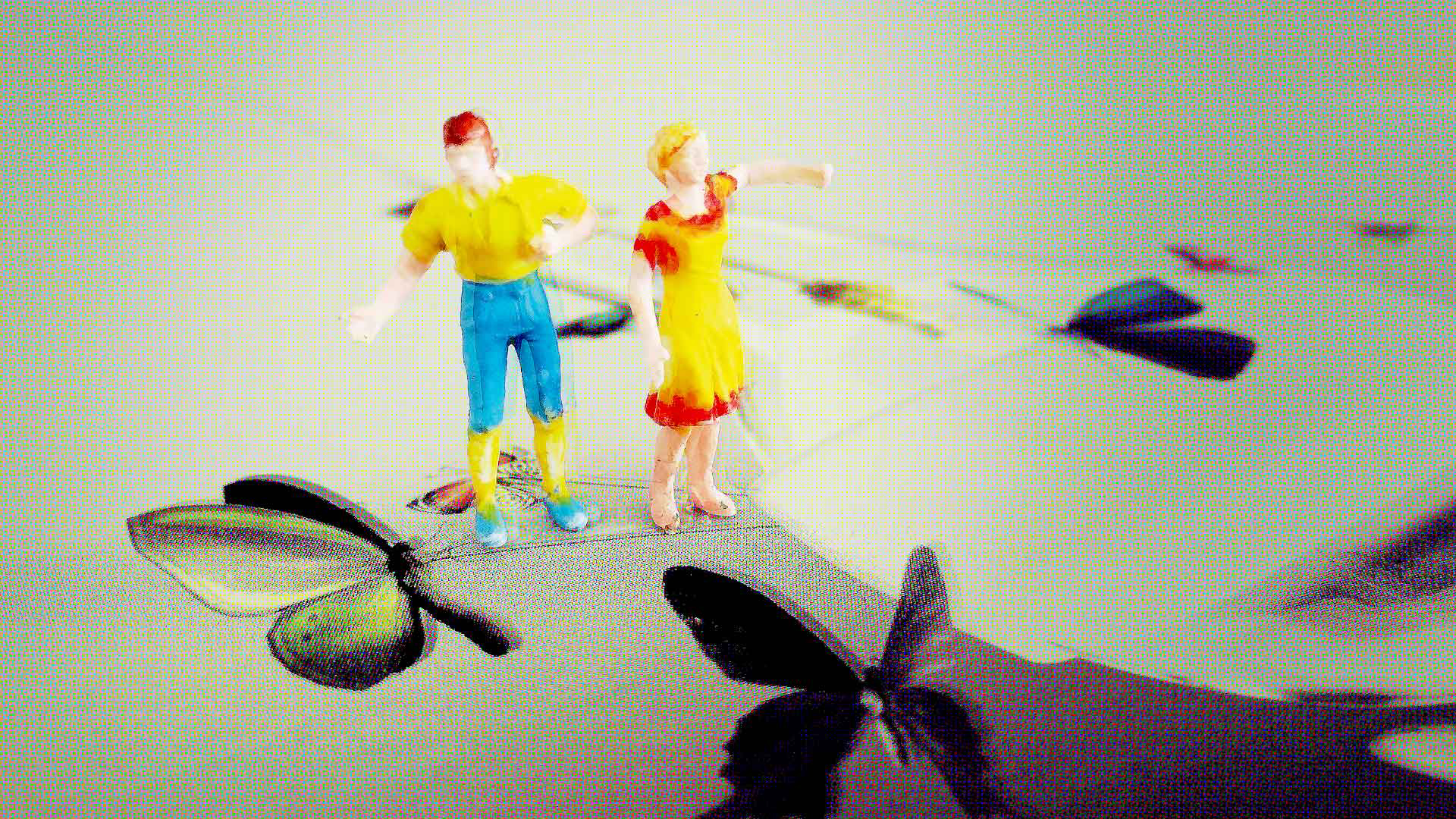 Zwei bunte Modellfiguren stehen auf einer Fläche mit Schmetterlingsmotiven; im unscharfen Hintergrund sind weitere grafische Formen zu sehen.