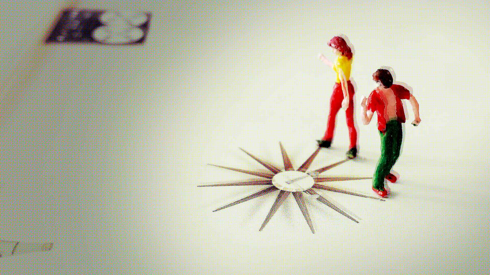 Zwei bunte Modellfiguren stehen neben einer sternförmigen Kompass-Rose auf einer hellen Fläche, im Hintergrund ist ein unscharfes Rechteck zu sehen.