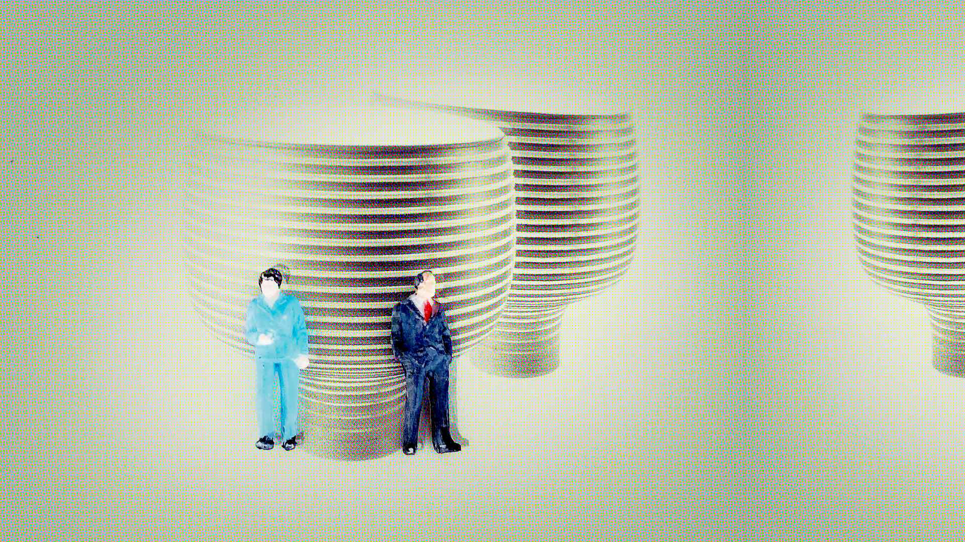 Zwei kleine Modellfiguren in Anzug und Overall lehnen vor grossen, gestapelten, gestreiften Gefässen in einer hellen Interior-Szene.