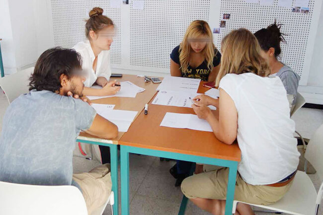Teilnehmer:innen der Sommerschule «Projects for Marrakech – Learning from each other» sitzen in einer kleinen Gruppe um einen Tisch und entwickeln gemeinsam Designkonzepte, notieren Ideen und diskutieren Skizzen, Marrakech 2015.