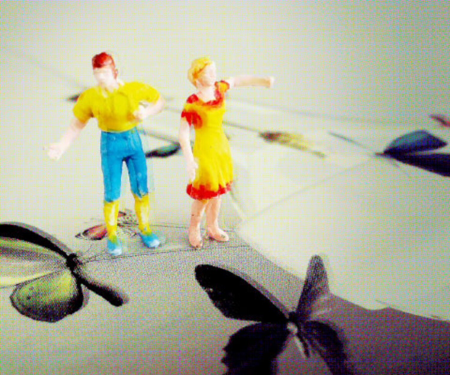 Zwei bunte Modellfiguren stehen auf einer Fläche mit Schmetterlingsmotiven; im unscharfen Hintergrund sind weitere grafische Formen zu sehen.