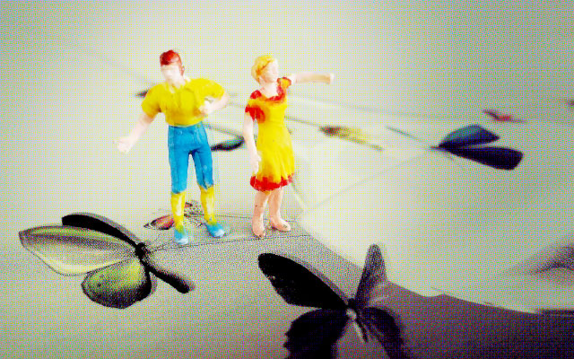 Zwei bunte Modellfiguren stehen auf einer Fläche mit Schmetterlingsmotiven; im unscharfen Hintergrund sind weitere grafische Formen zu sehen.
