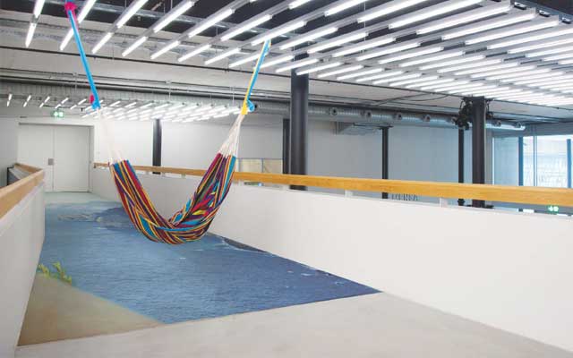 Farbige Hängematte auf der Passerelle im Toni-Areal, schräg in den Raum gespannt, darunter eine blaue Bodeninstallation, die den grauen Korridor in eine maritime Traumlandschaft verwandelt.