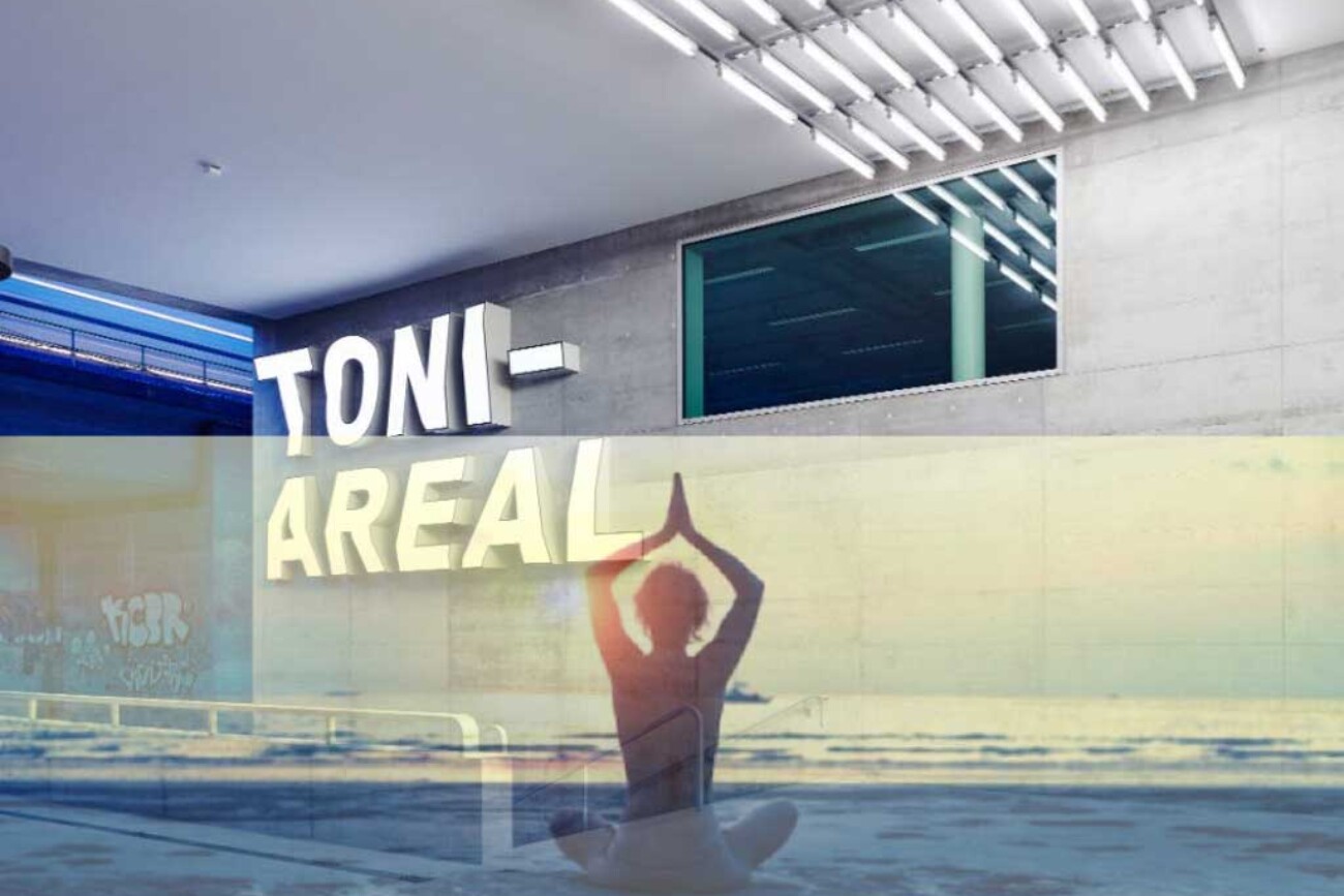 Fotomontage am Eingang des Toni-Areals: über dem Betonbau mit Leuchtschrift „TONI-AREAL“ erscheint halbtransparent die Silhouette einer meditierenden Person am Strand, als würde das Hochschulgebäude zur Thermalbad- und Strandkulisse werden.