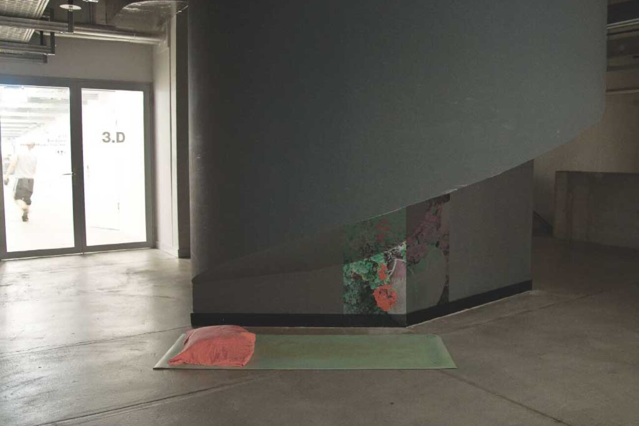 Meditationsplatz im Toni-Areal mit grüner Matte und rosafarbenem Kissen vor einer dunklen Betonstruktur, unten von einer farbigen Pflanzeninstallation aufgehellt, als ruhige Insel in der Gebäudeecke.