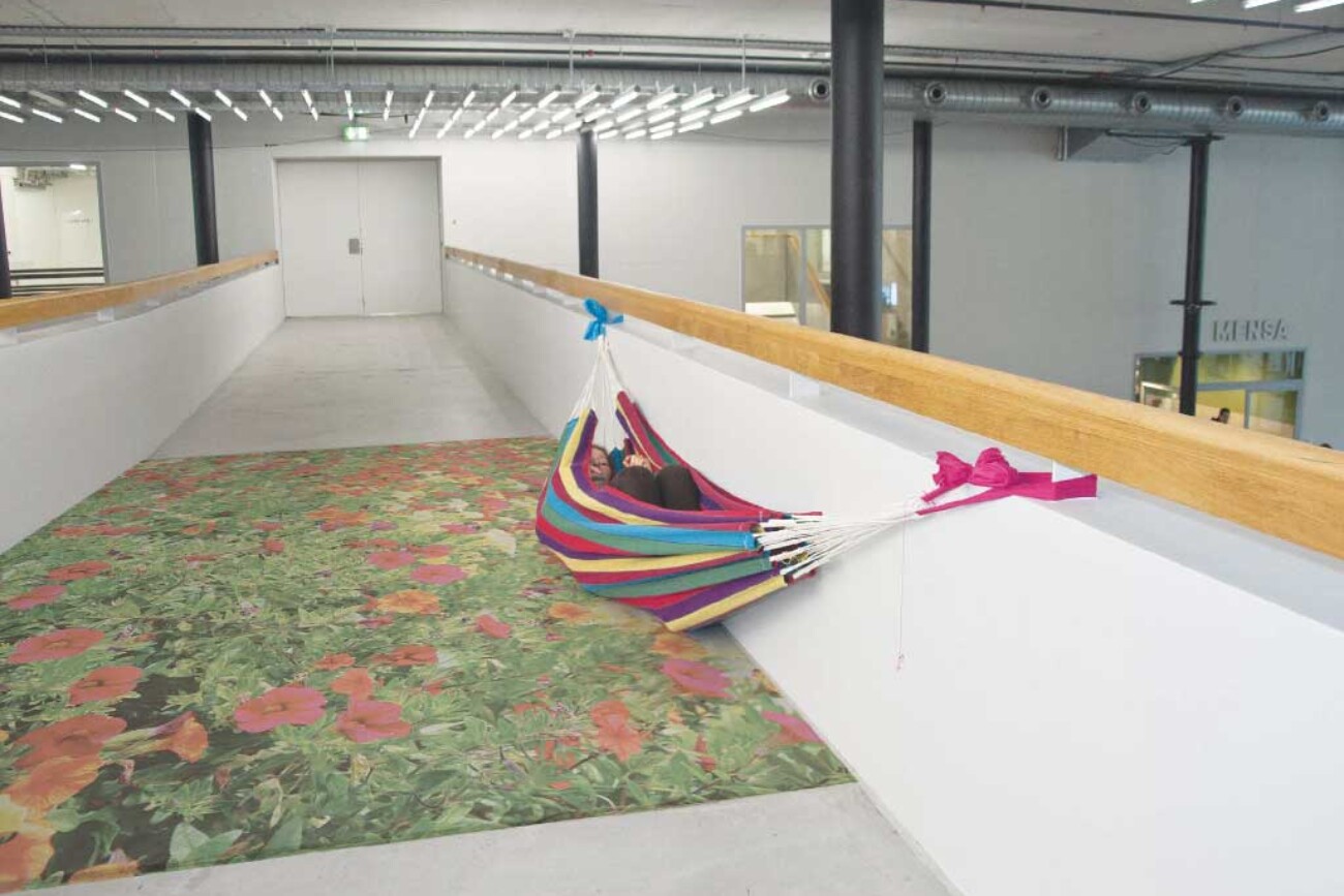 Farbige Hängematte mit liegender Person, installiert auf der Passerelle im Toni-Areal, deren Boden durch eine grossflächige Blumeninstallation in eine traumartige Insel verwandelt wird.